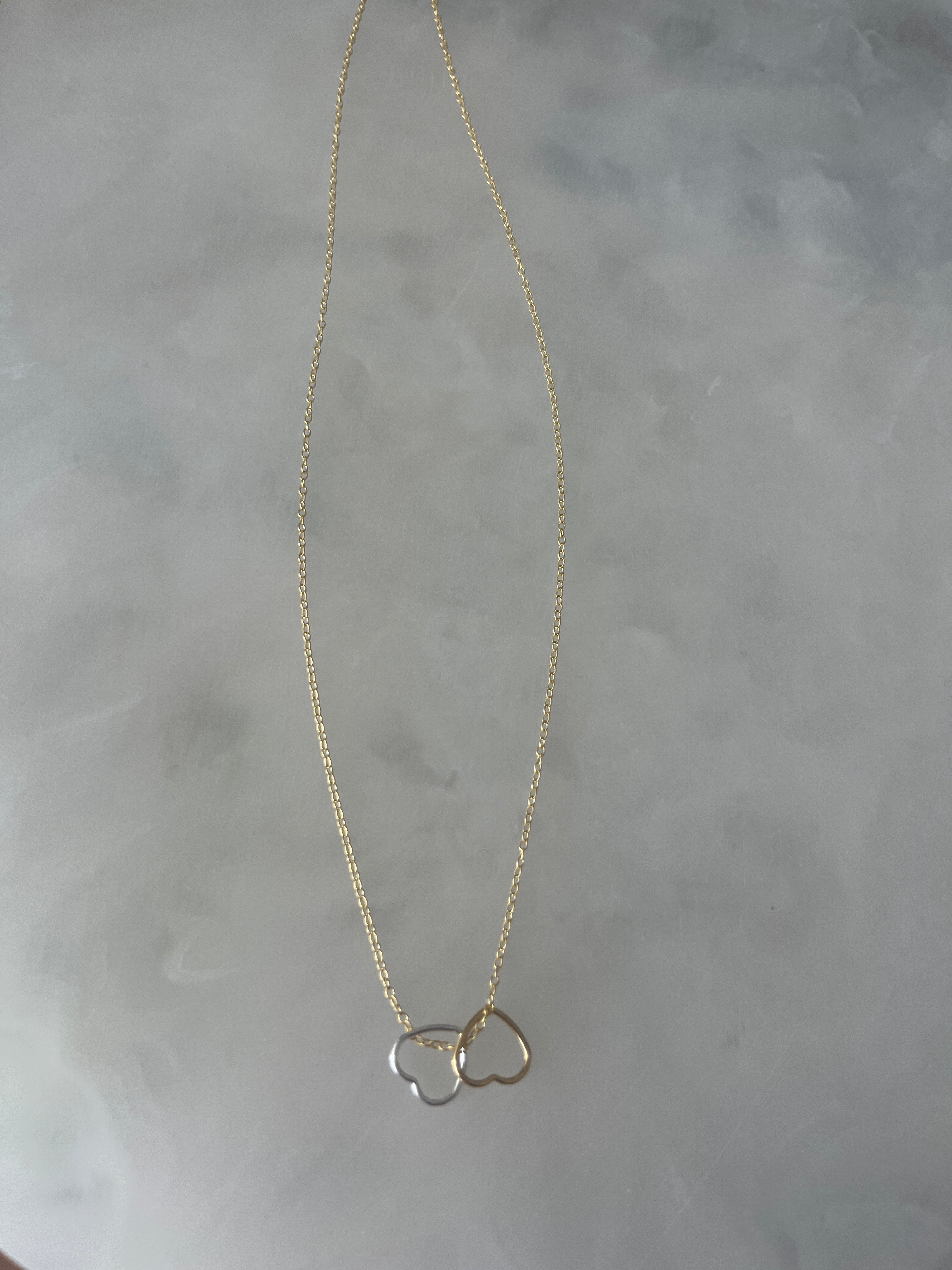 Two open hearts, gold and silver together on gold chain necklace.